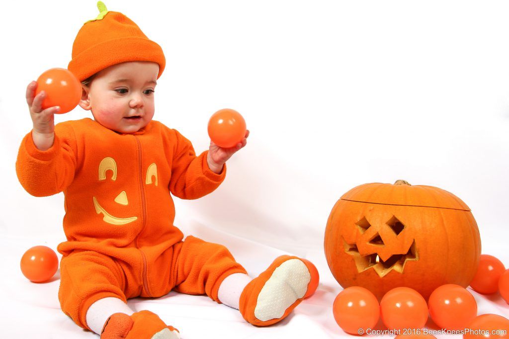 baby playing with orange balls and a pumpkin at a halloween photoshoot