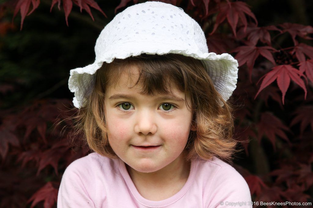 young girl in a white hat in front of a red bush