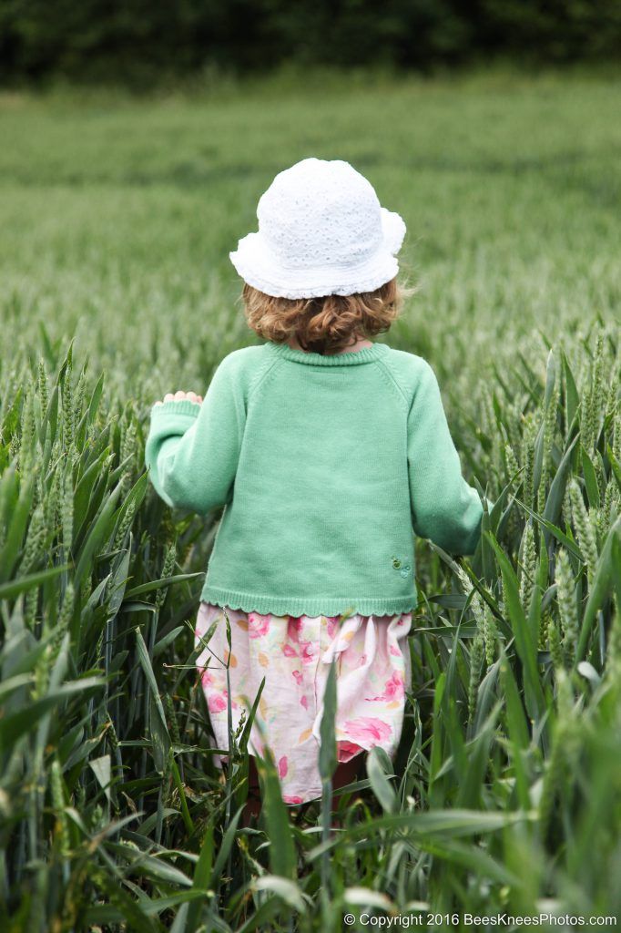 young girl wallking through a cornfield in a green dress